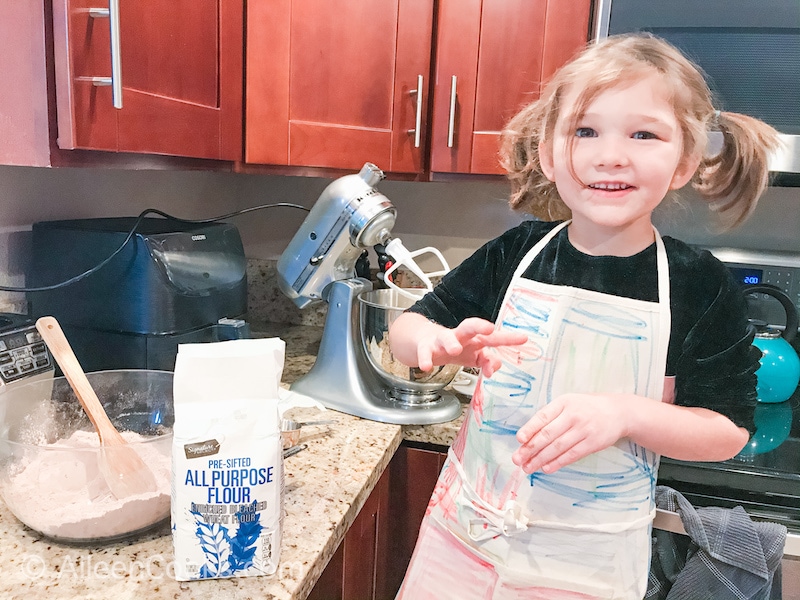 A little girl in an apron, helping to make red velvet cookies.