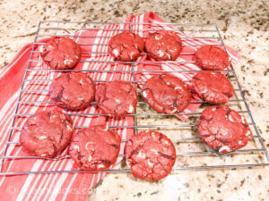 Red velvet cookies cooling on a metal cooling rack over a red and white striped towel.