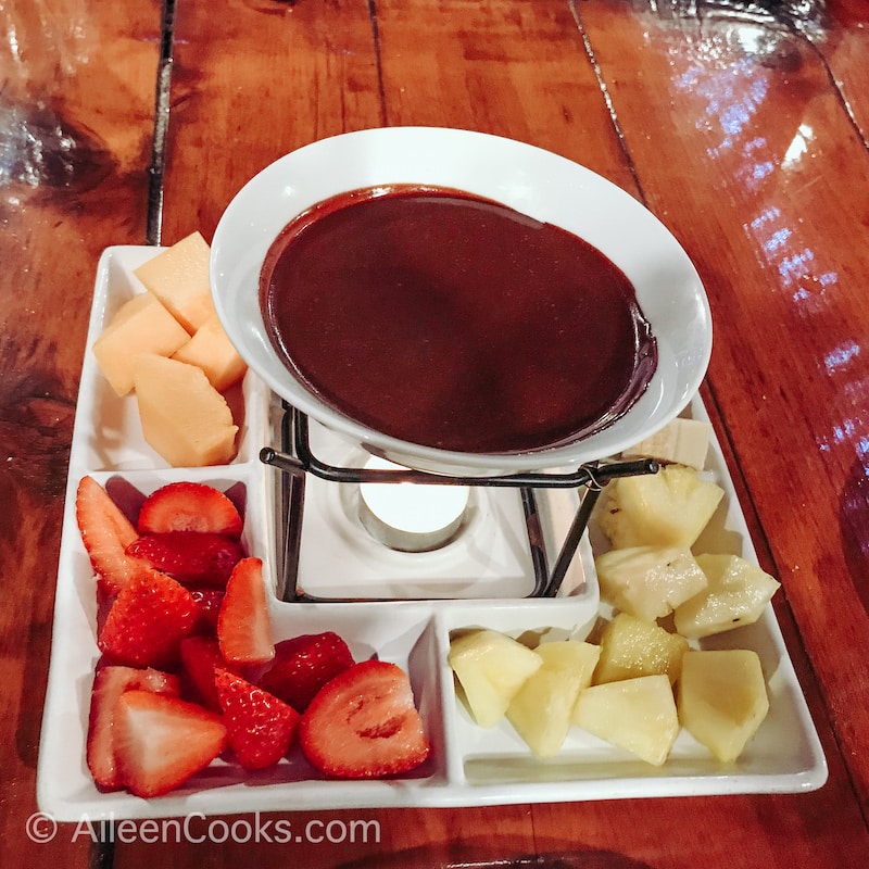 A bowl of chocolate fondue surrounded by cut up fruit.