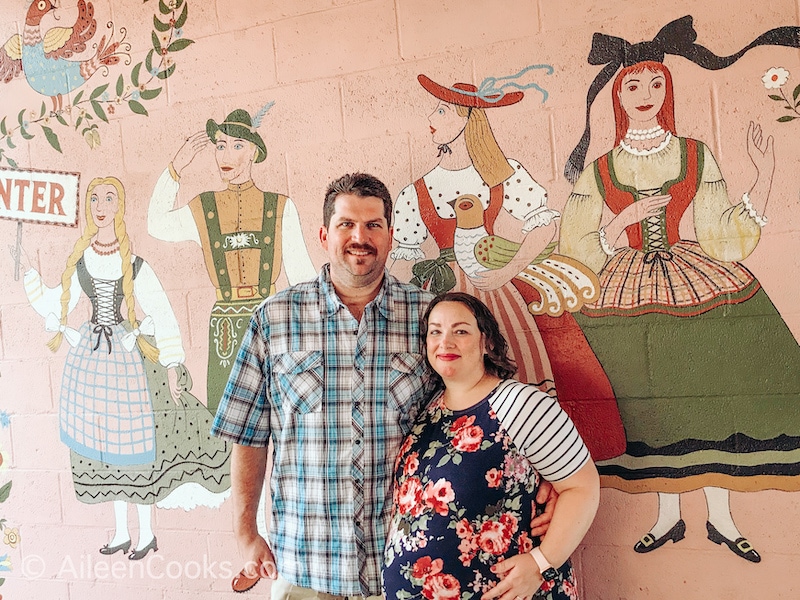 A man and woman standing in front of the mural at Hofas House Hotel.