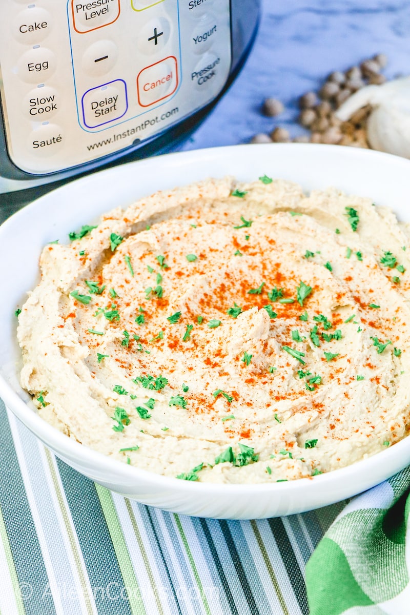 A white bowl of hummus in front of an instant pot.