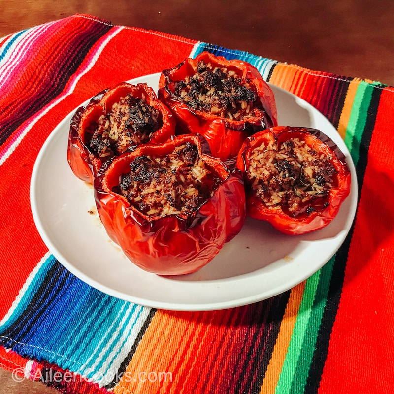 Four stuffed peppers on a white plate, on top of a striped tablecloth.