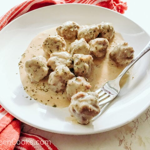 A white plate of Swedish meatballs with one meatball on a fork.