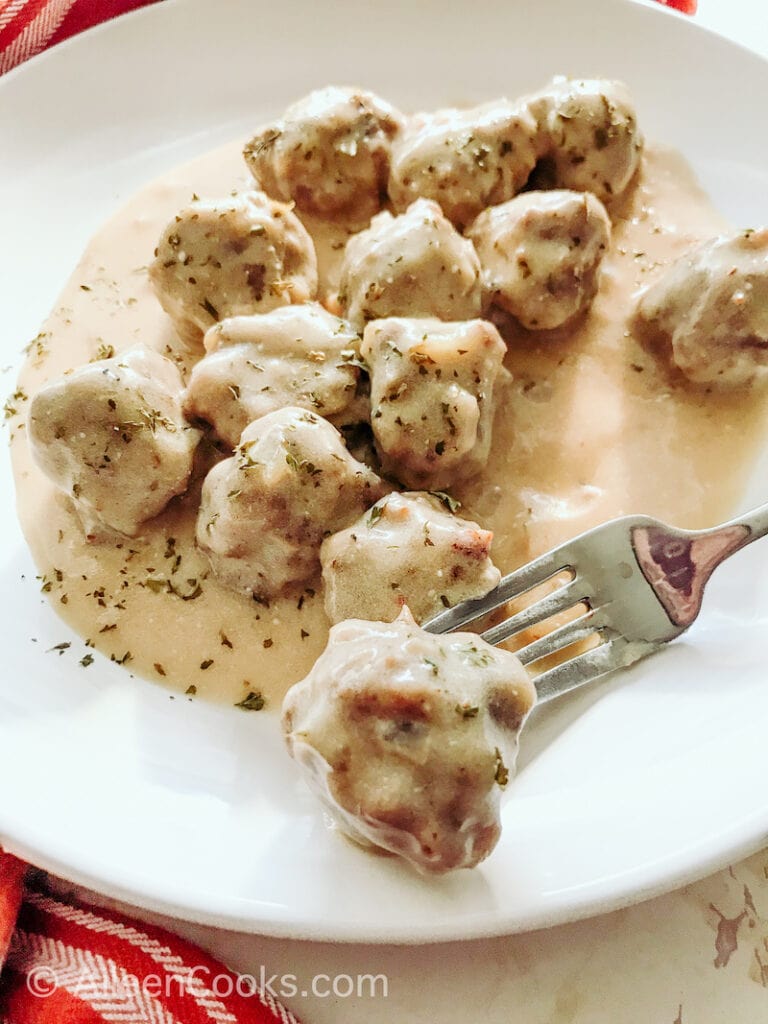 Close up of Swedish meatballs on a plate with fork resting on plate holding meatball.