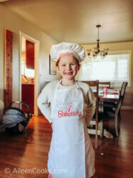 A girl wearing a white apron and hat that say "Baketivity" on them.