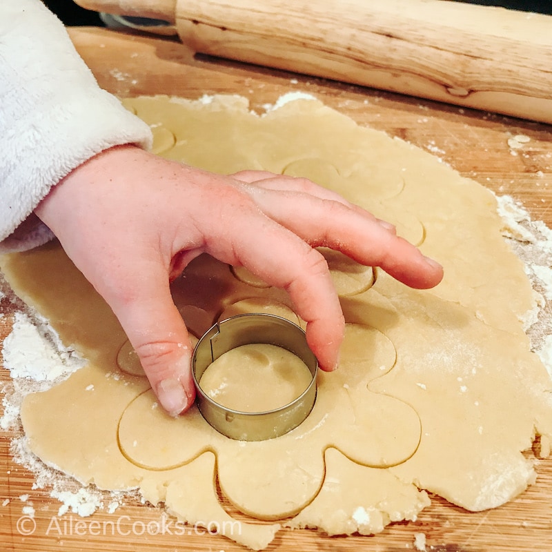 A hand pressing a cookie cutter into rolled-out cookie dough.