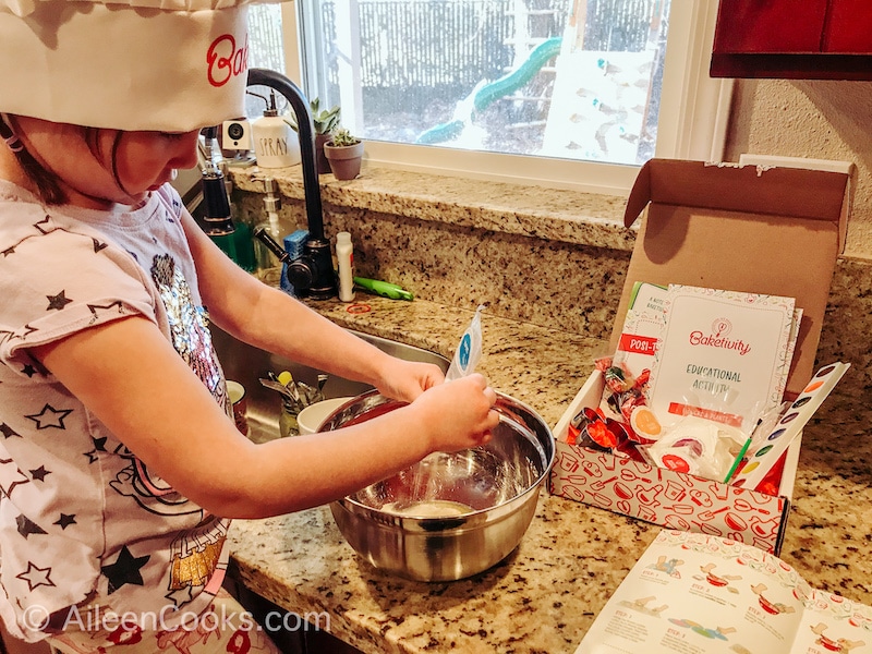 A little girl stirring cookie dough in a metal bowl.