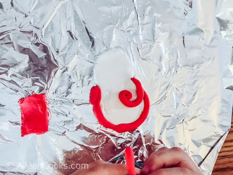 A piece of foil with white and red air dry clay shaped into a Maori charm.