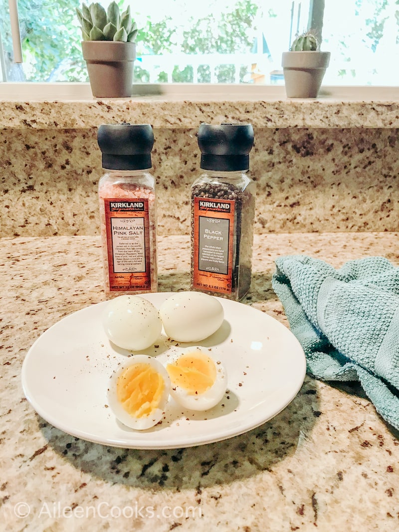 A plate of hard boiled eggs in front of salt and pepper grinders.