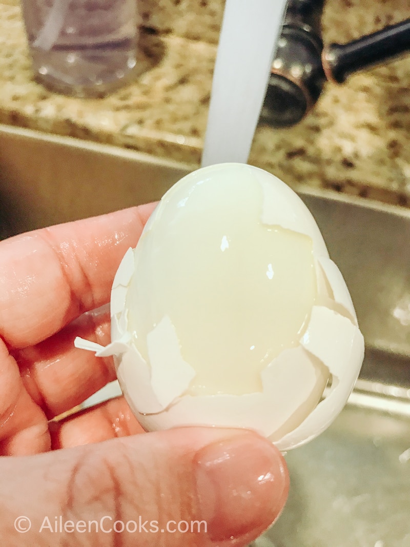 A hard boiled egg being peeled under running water.