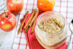A jar of overnight oats next to apples and cinnamon sticks.