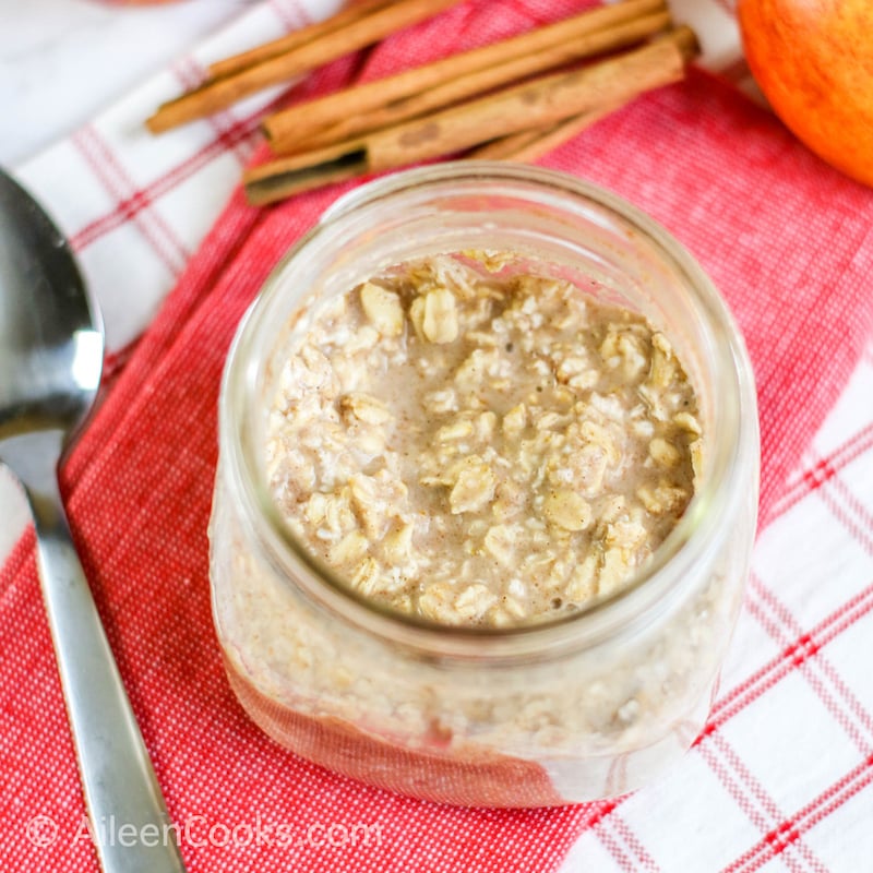 A jar of overnight oats next to cinnamon sticks and a spoon.