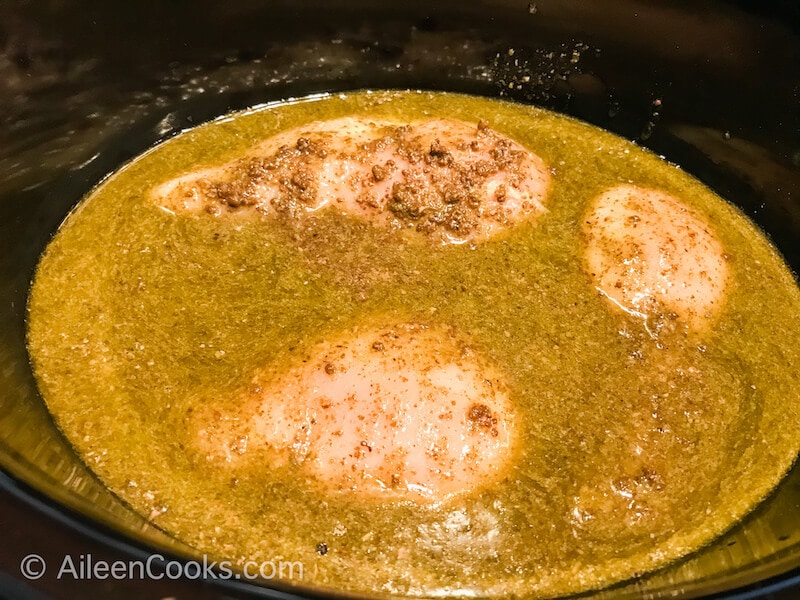 Chicken covered with pesto and chicken broth, inside of a crockpot.