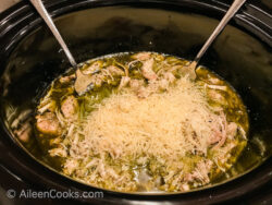 Parmesan cheese on top of a shredded pesto chicken inside a slow cooker.