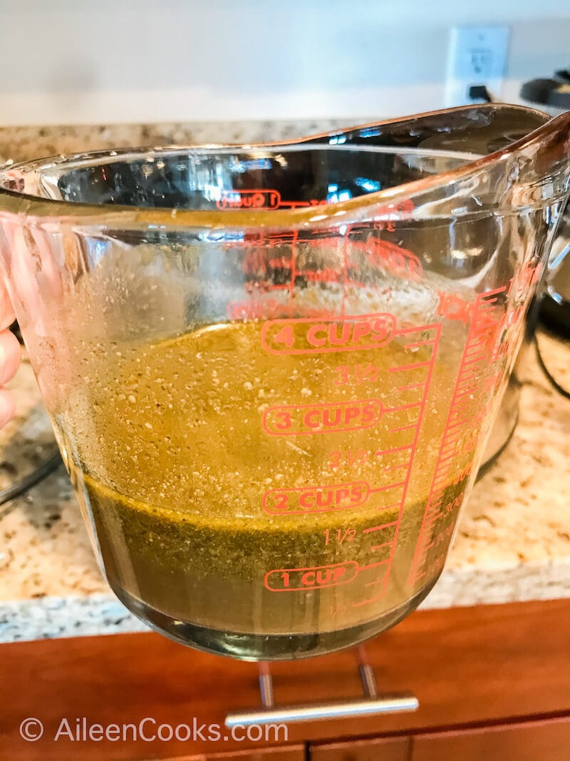 Pesto and chicken broth mixed together in glass measuring cup.