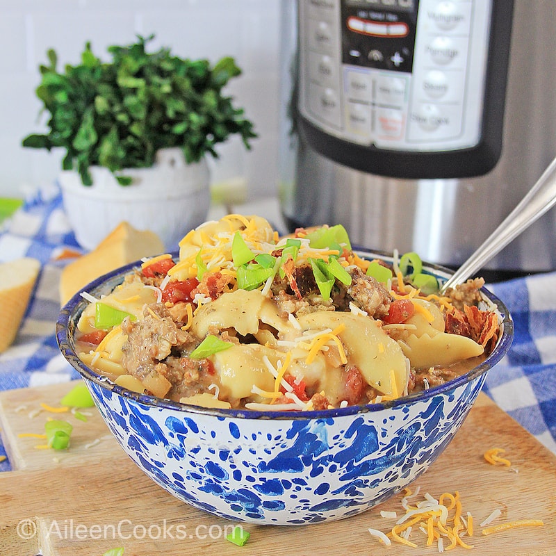 A blue floral bowl filled with tortellini soup with an instant pot and bowl of cilantro in the background.