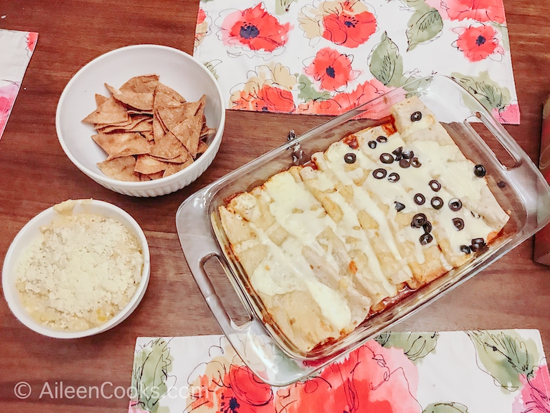 Overhead shot of enchiladas, corn dip, and homemade tortilla chips on a wooden table.