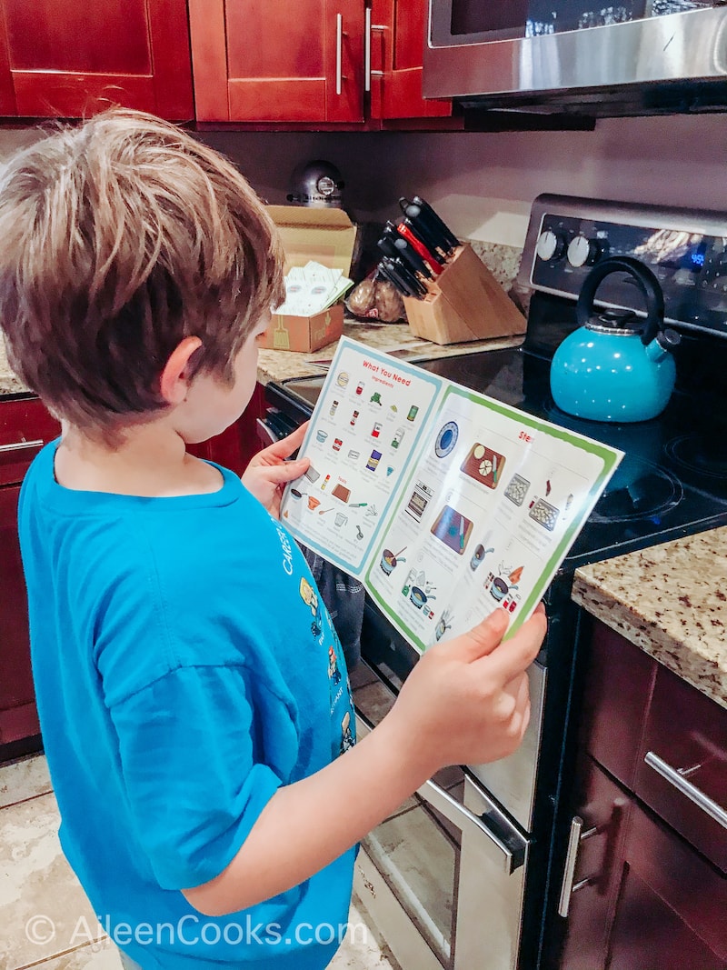 A boy in a blue shirt reading a recipe card.