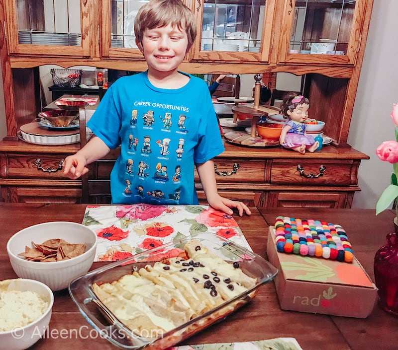 A boy in a blue shirt pointing at a bowl of homemade tortilla chips.