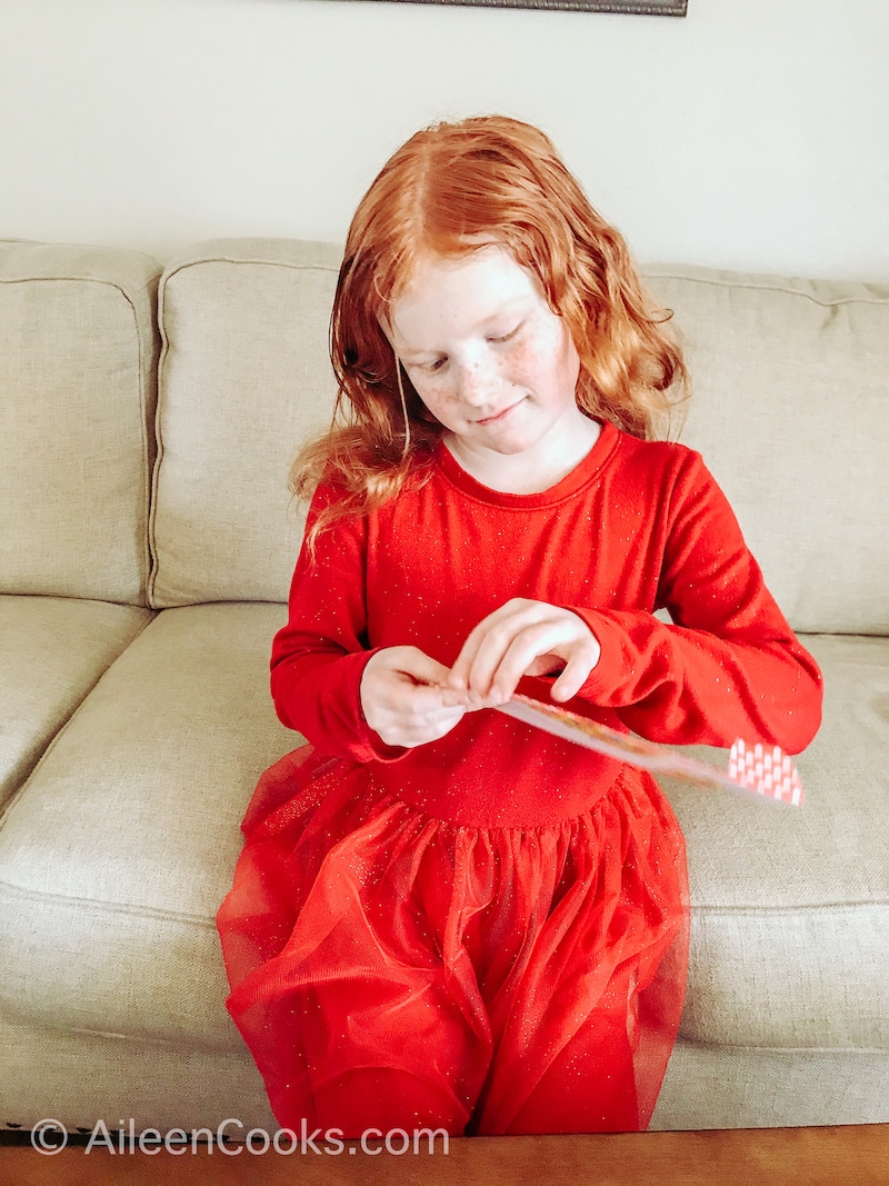 A little girl sitting on a couch, opening a yellow envelope.