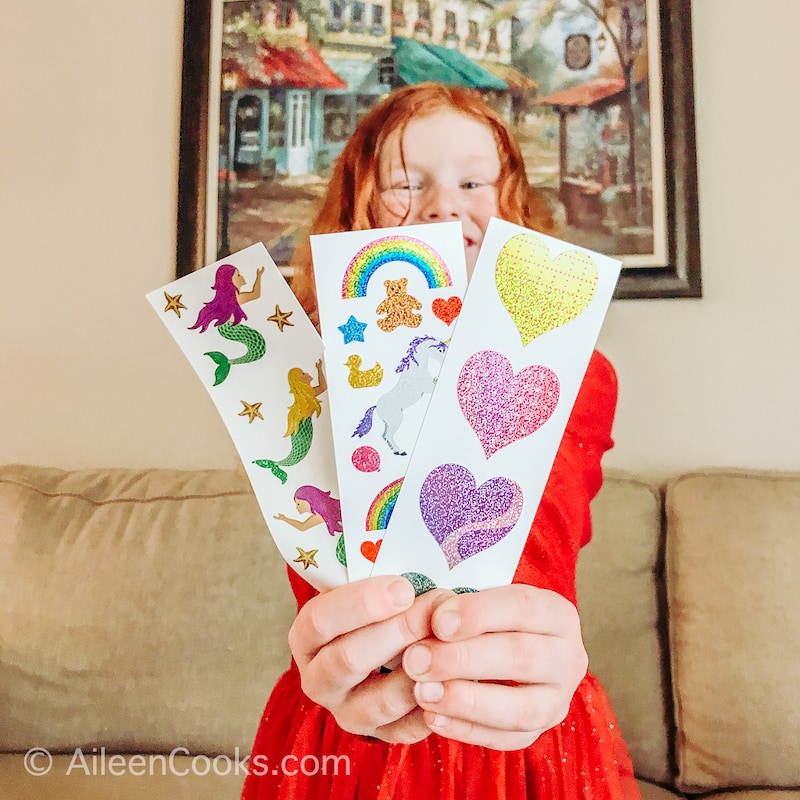 A little girl holding up three sheets of stickers.