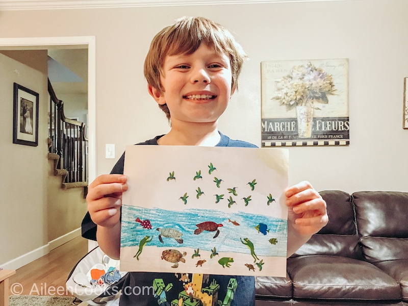 A boy holding up a picture decorated with stickers.