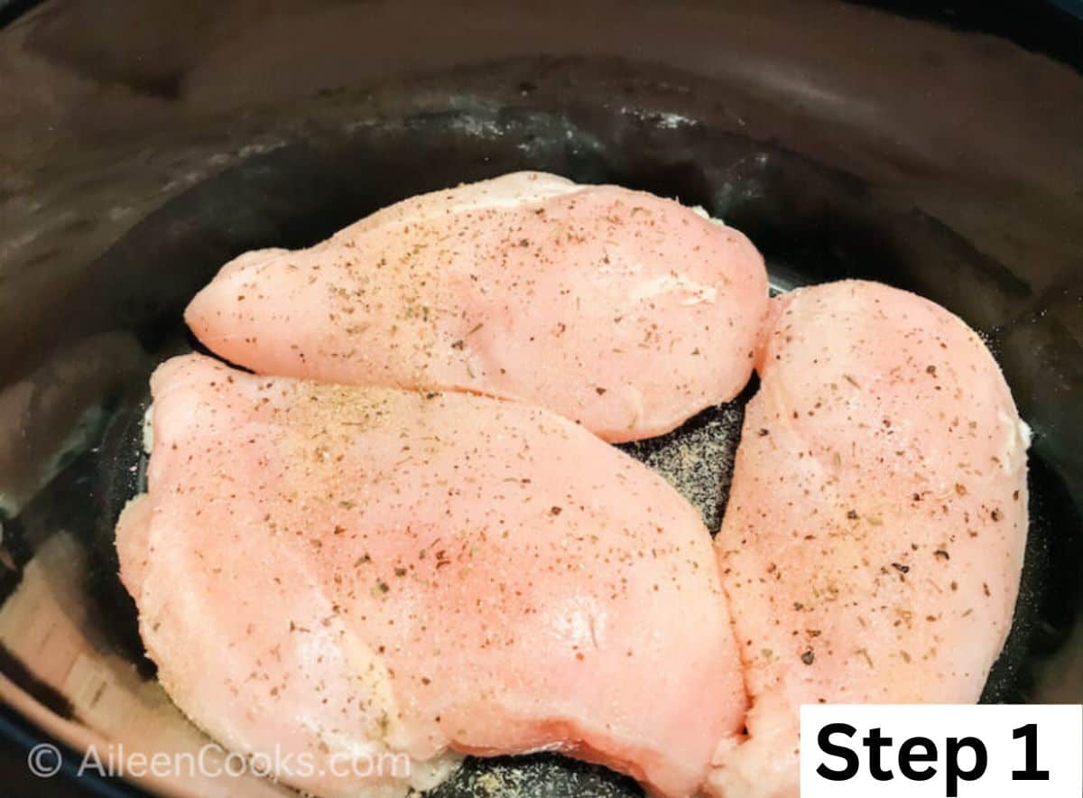 Three seasoned chicken breasts inside a slow cooker.