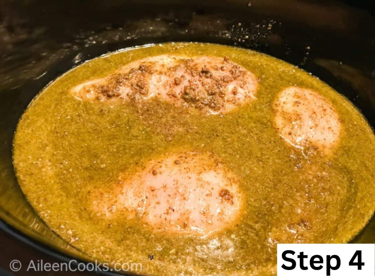 Chicken and pesto inside of slow cooker.