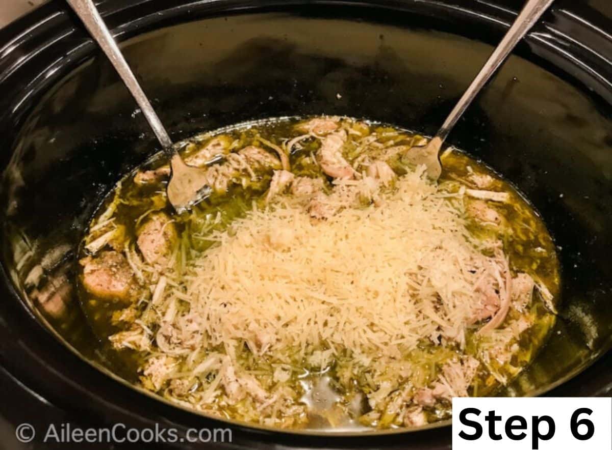 Pesto chicken inside of a slow cooker and topped with shredded parmesan cheese.