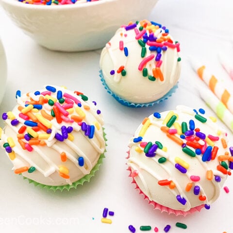 Three white chocolate bombs sitting on colorful muffin cups.