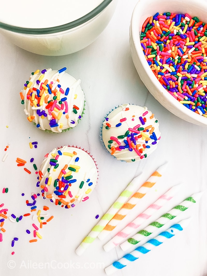 Three white hot cocoa bombs covered in rainbow sprinkles.