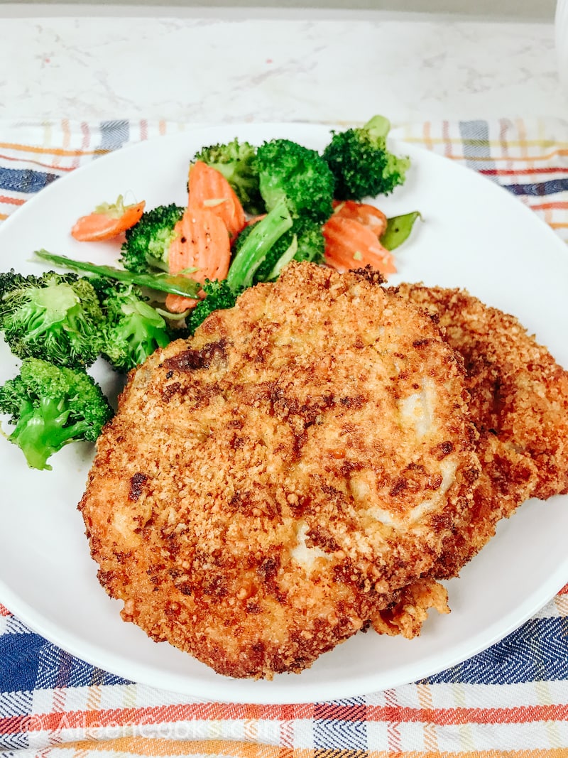 A white plate of breaded pork chops, broccoli, and carrots.