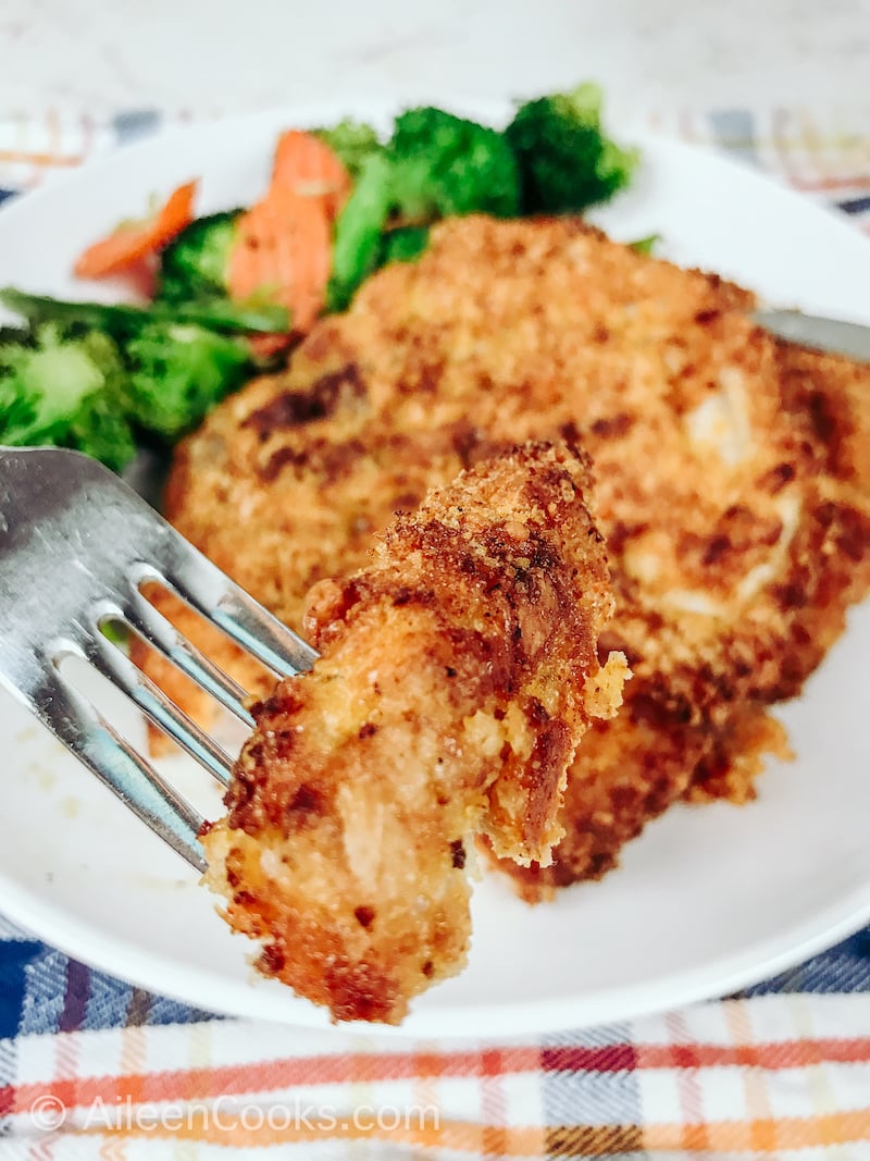 A fork holding a bite of breaded pork chops.