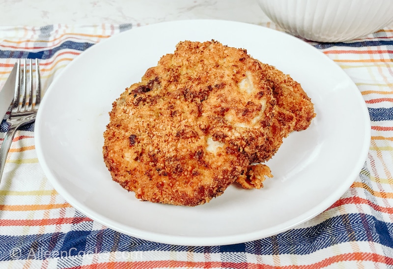 Two breaded pork chops on a white plate.