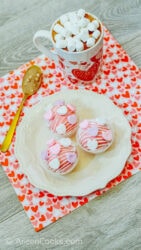 Three hot cocoa bombs on a white plate, on top of a Valentine's Day placemat.