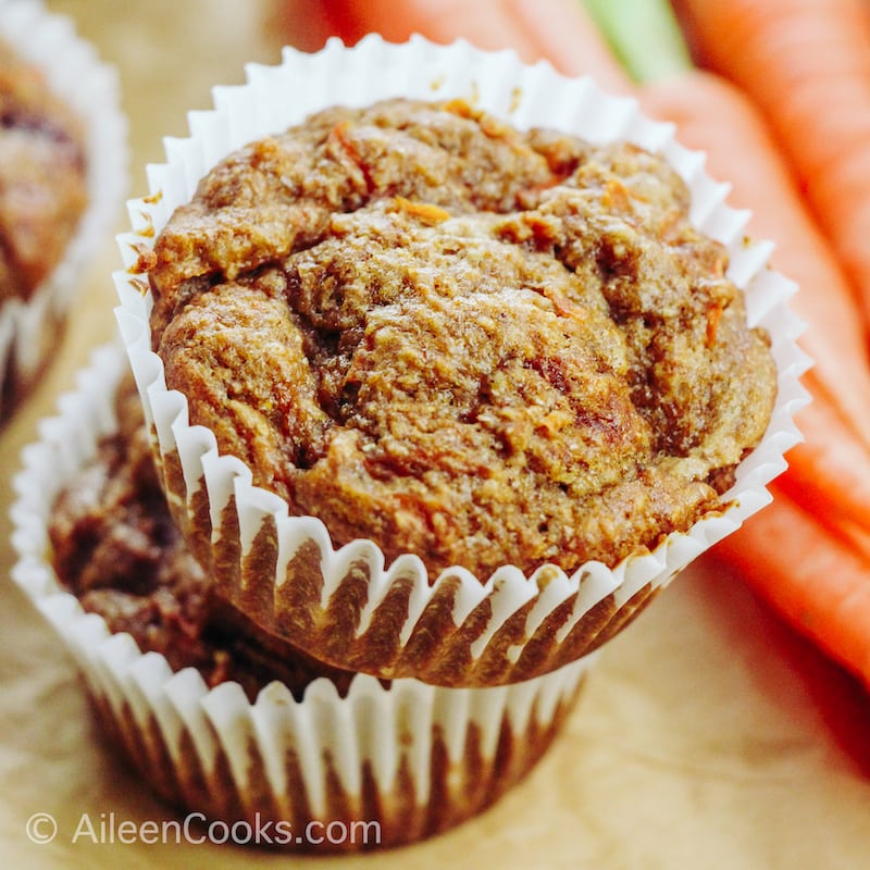 A stack of two carrot muffins next to fresh carrots.
