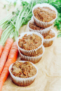 A large bunch of carrots next to stacked up carrot muffins.