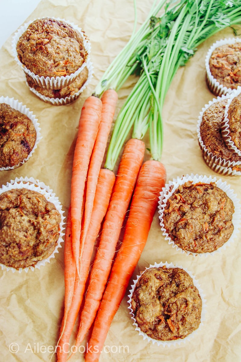 A bunch of carrots surrounded by healthy carrot muffins.