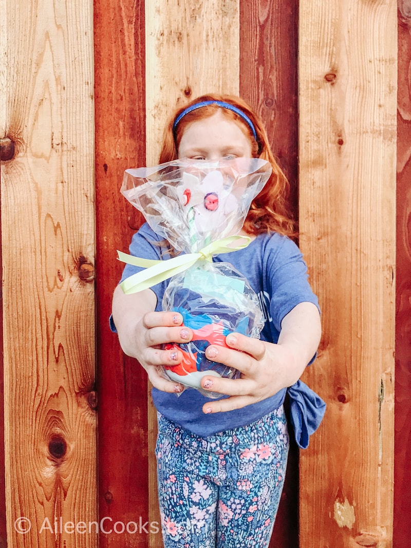 A red-haired girl holding out a homemade vase wrapped in plastic.