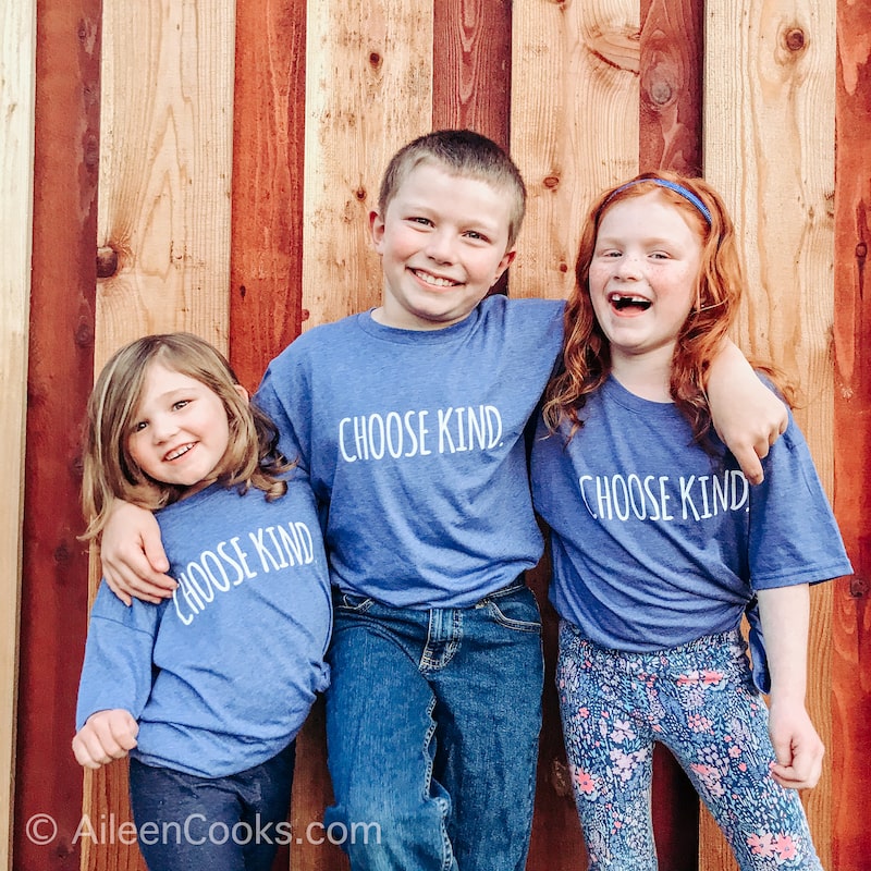 Three kids standing in front of a wooden fence, 