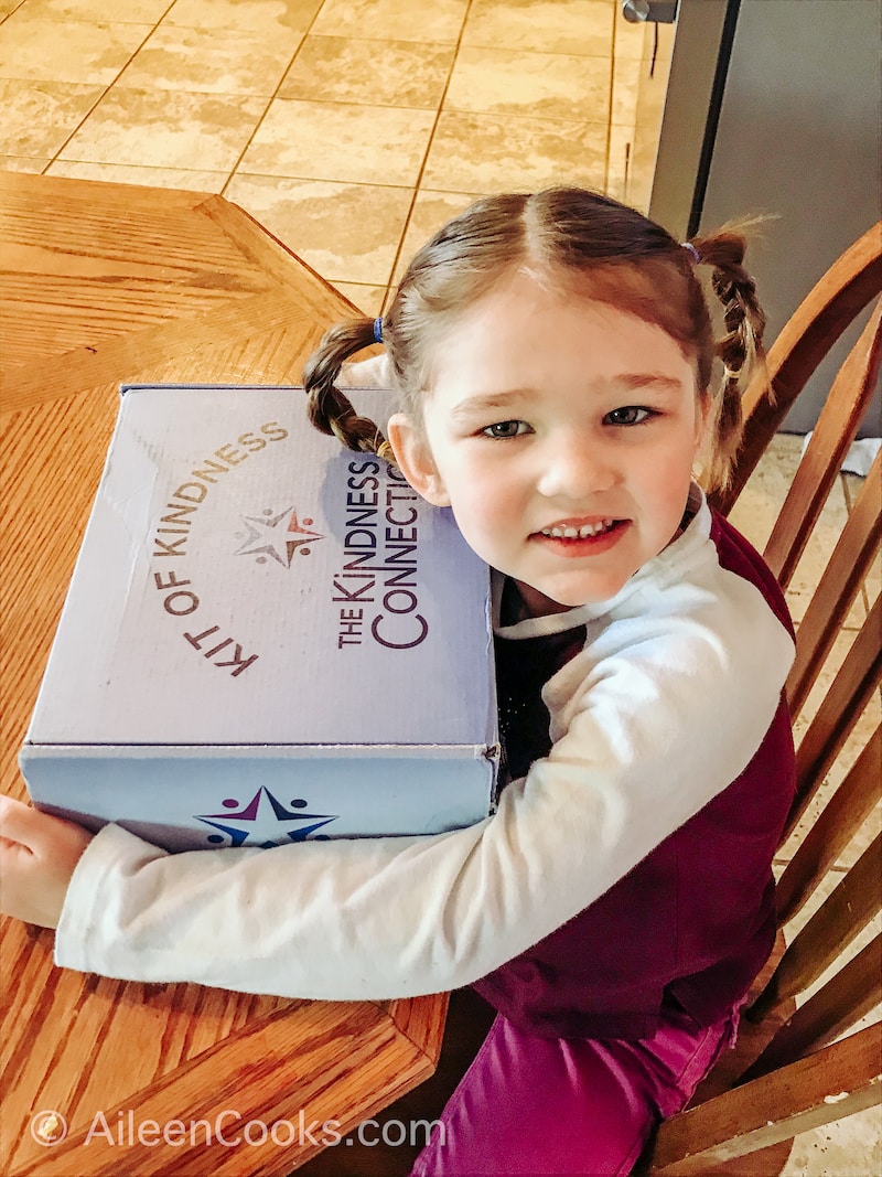 A little girl holding a blue box that says kindness connection.