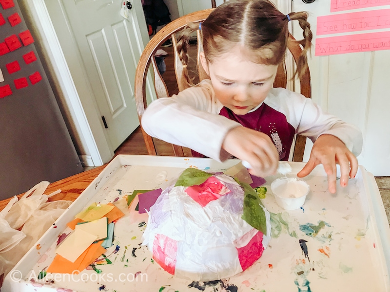 A little girl decorating a plastic bowl with tissue paper.