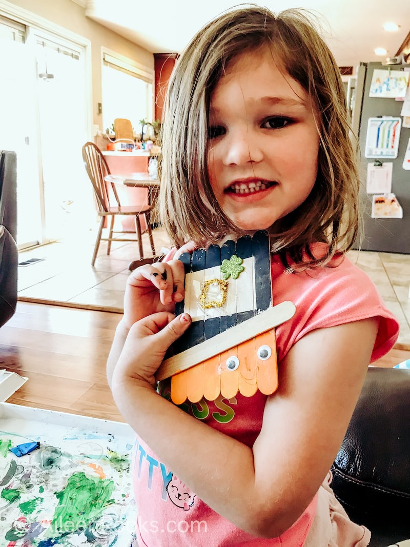 A little girl holding up a completed leprechaun Popsicle stick craft.