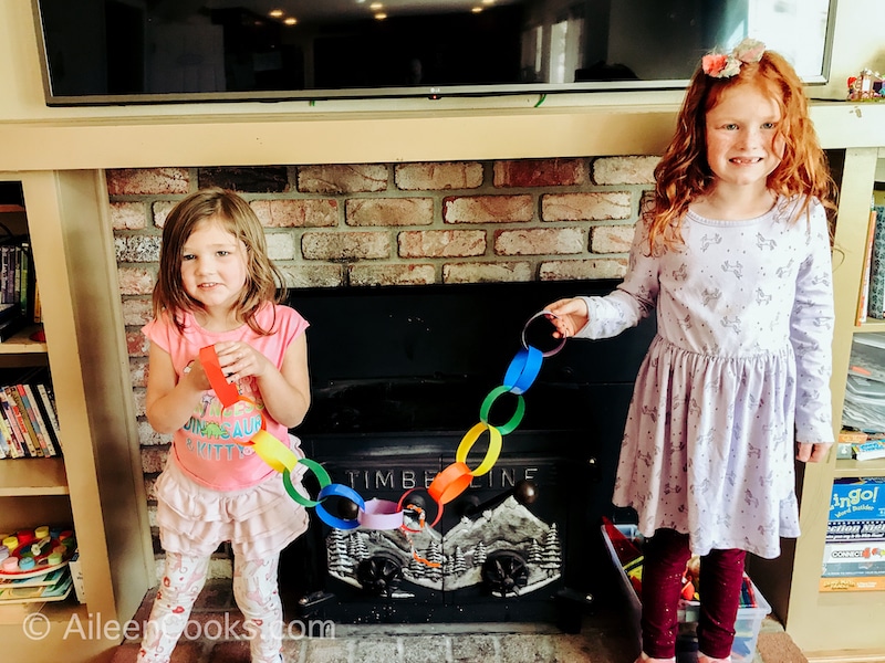 Two little girls holding up a rainbow paper chain.