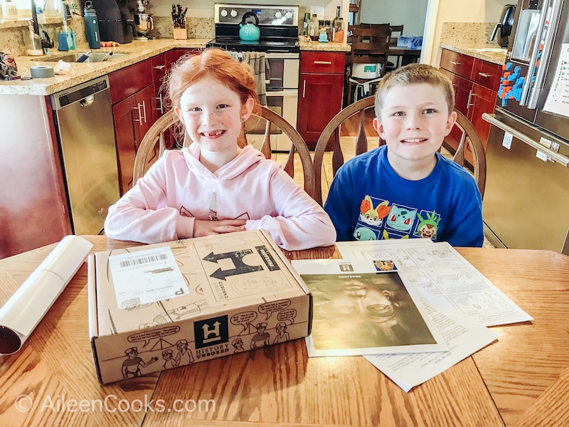 A boy and girl sitting at a table with a History Unboxed subscription box in front of them.