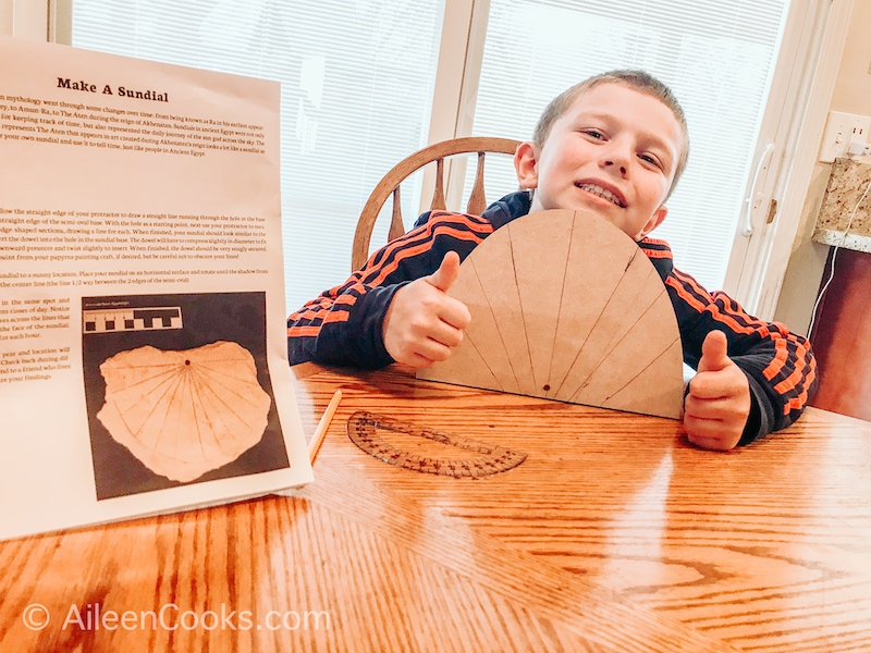 A boy holding up a completed sundial with a thumbs up.