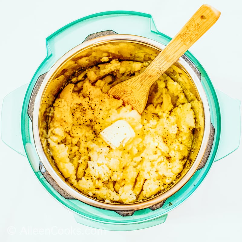 Teal instant pot filled with mashed potatoes and wooden spoon.