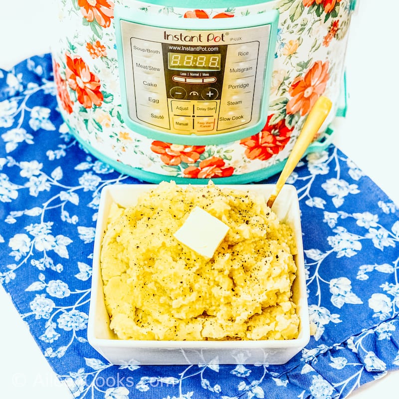 A square bowl of mashed potatoes in front of a floral instant pot.