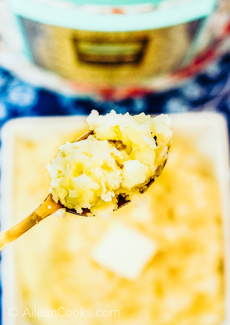 A spoonful of mashed potatoes held above a bowl of mashed potatoes.