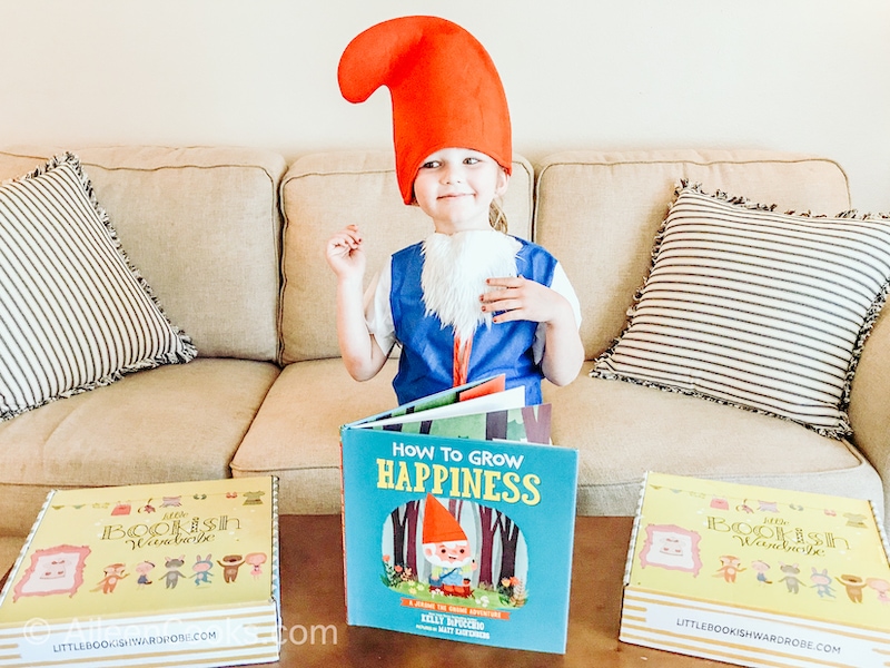 A little girl dressed as an elf with a children's book called How to Grow Happiness.